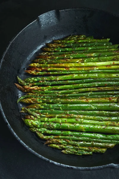 koyu taş arka plan üzerinde Dökme demir tavada yağ ve baharat ile kavrulmuş kuşkonmaz. Vegetfrian ve vegan gıda pişirme. Üst viev
