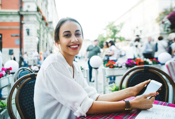 Atractiva mujer sonriente sentada en la cafetería de la calle usando el teléfono — Foto de Stock