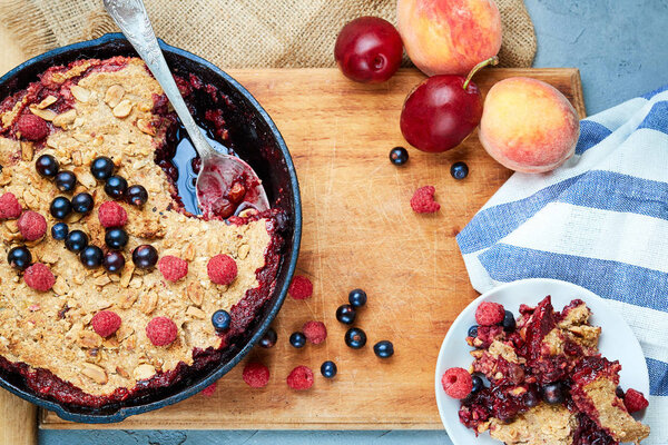 Food background. crumble with blueberries in the black cast-iron frying pan on the wooden cutting board with fruits and napkin . Top view