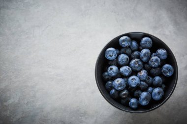 karanlık bir beton zemin üzerine siyah bir kase taze yaban mersini