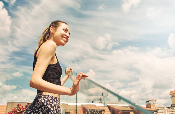 attractive happy smiling woman posing on the amazing cloudy blue sky background in the center of old city of Lviv. woman admires the view of the cityscape from the rooftop with wonderful cloudy blue sky on background