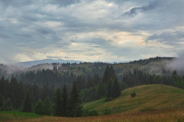 Karpat orman ve dağ manzara tatil evleri ile bulutlu akşamları. Sisli orman ve Ukraynalı dağlarda bulutlu gökyüzü