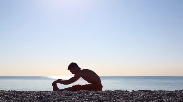 Egy fiatal férfi megfelel a hajnal, és nem a tenger strandon jóga — Stock videók
