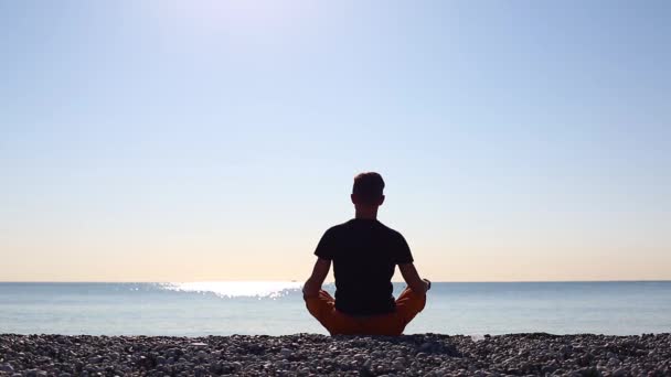 Ein junger Mann trifft die Morgendämmerung und macht Yoga am Meeresstrand — Stockvideo