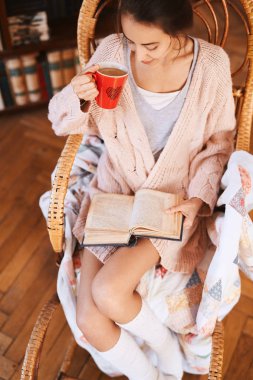 Kadın bir hasır sandalye eski kitap ve kahve ile yumuşak fotoğrafı. Rahat örgü pembe kazak ve beyaz diz çorap giyen kadın.
