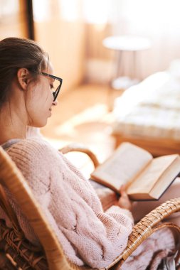 Kadın bir hasır sandalye eski kitap ve kahve ile yumuşak fotoğrafı. Rahat örgü pembe kazak ve beyaz diz çorap giyen kadın.