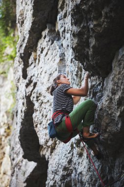Kız kaya tırmanışçısı parlak yeşil yan görünüm cliff üzerinde tırmanma pantolon. kaya tırmanışçısı kayalık bir duvara tırmanıyor. kadın sert hareketi yapma