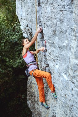 Genç ince kadın dağcı parlak turuncu üst yan görünüm cliff üzerinde tırmanma pantolon. kız bir dikey düz kayalık duvar ve sert hareket yapmadan tırmanıyor