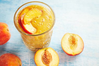 Sağlıklı yaz breackfast. Şeftali smoothies bir cam ve mavi ahşap masa üzerinde olgun şeftali yarısı. Sağlıklı, temiz yemek, vegan, Vejetaryen, detoks, diyet kahvaltı gıda kavramı