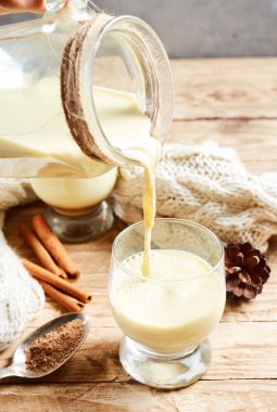 Cinnamonis bir sıcak Noel yumurta likörü bir sürahi bir cam içine dökülür üzerinde ahşap masa lambası