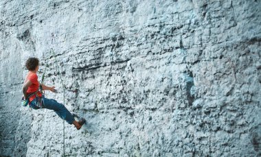 Genç adam kaya tırmanışçısı cliff üzerinde tırmanma parlak mavi pantolon içinde arka yan görünüm. kaya tırmanışçısı kayalık bir duvara tırmanıyor. sert yapma adam zorlu rotada hareket