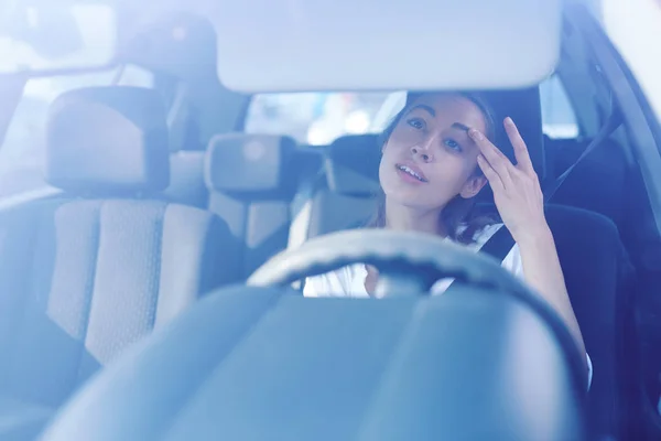 Motorista mulher olhando para o espelho retrovisor e corrigindo o penteado e maquiagem durante a condução do carro — Fotografia de Stock