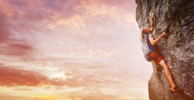 Genç adam kaya tırmanışçısı parlak kırmızı şort ve zorlu yol cliff üzerinde tırmanma mavi tişört giyiyor uzun saçlı parlak görüntü. kaya üzerinde bir kireçtaşı duvara tırmanma tırmanıcı