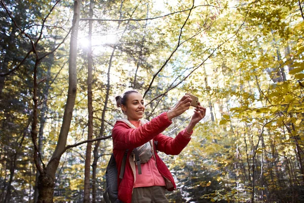 Feliz mujer sonriente en una chaqueta roja caminando en el bosque de otoño — Foto de Stock