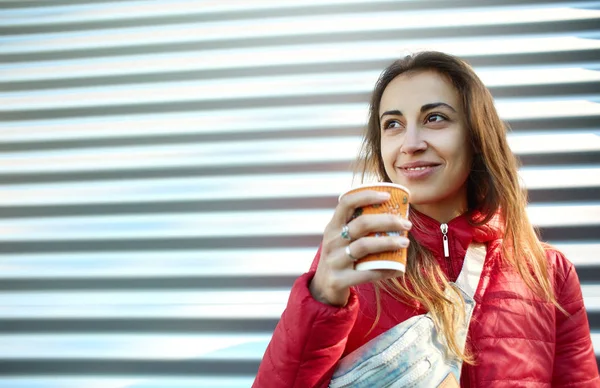 Young woman in red jacket with blue jeans Waist bag drinking coffee outdoors — Stock Photo, Image