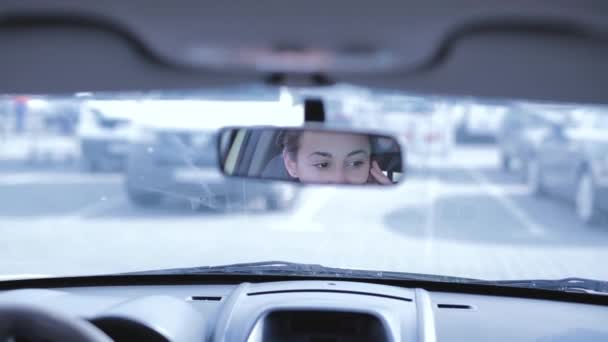 Mujer morena hablando en un teléfono celular mientras conduce un coche. visión trasera a través del espejo retrovisor — Vídeos de Stock