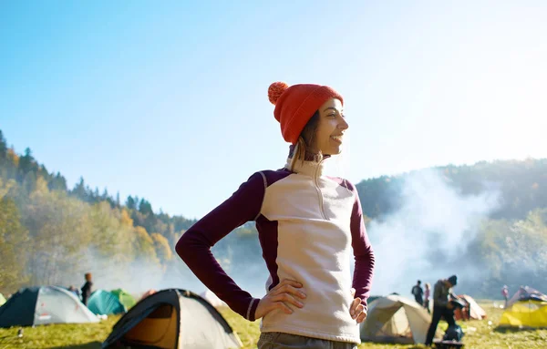 Onnellinen hymyilevä nainen punaisessa hatussa seisoo leirintäalueella syksyllä metsässä — kuvapankkivalokuva