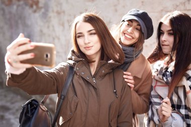 Sonbaharda cep telefonunda üç neşeli kız arkadaş selfie çekiyor. Genç şık kız güneşli sonbahar gününde iki kız arkadaşıyla selfie çekiyor.