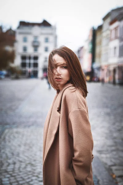 Молодая женщина в коричневом пальто позирует на улице — стоковое фото