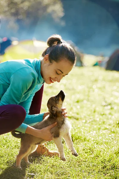 Ung kvinna som leker med en söt liten valp på ett grönt gräs i Camping — Stockfoto