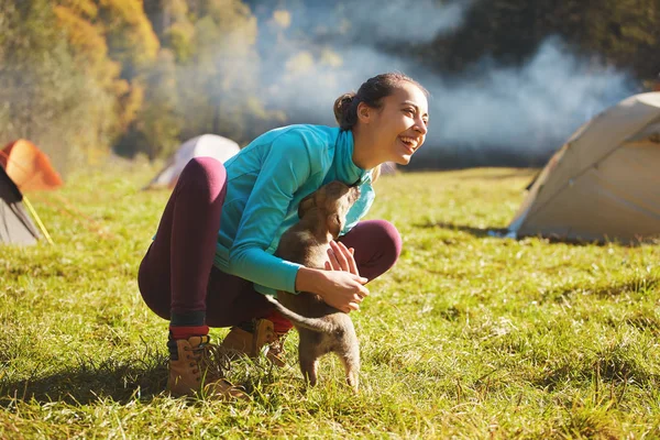 Ung kvinna som leker med en söt liten valp på ett grönt gräs i Camping — Stockfoto