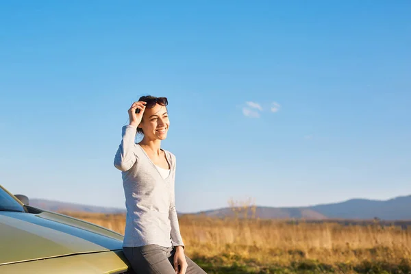 Atractiva mujer sonriente está de pie en la carretera cerca del coche — Foto de Stock