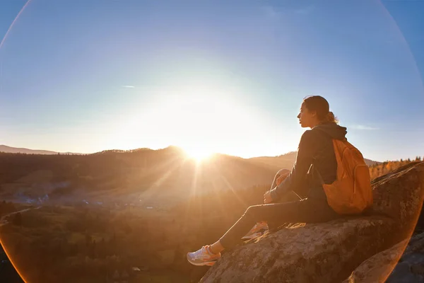 Жінка сидить на краю скелі на фоні сходу сонця — стокове фото