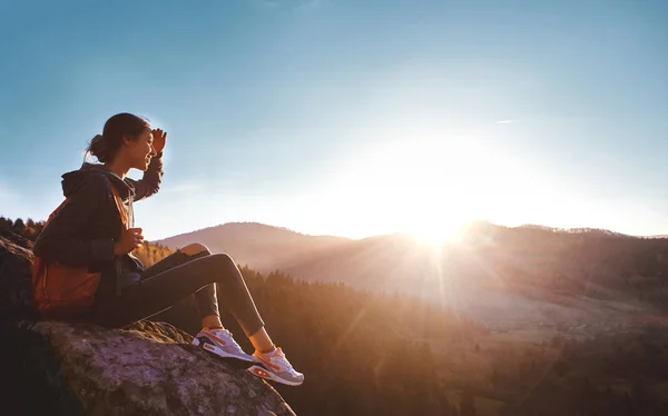 Woman sits on edge of cliff against background of sunrise — Stock Photo, Image