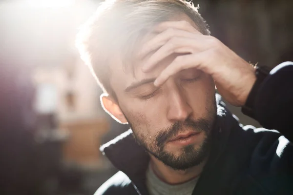 Close-up portret van een jonge baard huilende man staande in backlight op de straat — Stockfoto