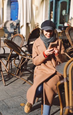 kahverengi ceket ve gri kapak genç kadın Sokak kafede masada oturuyor