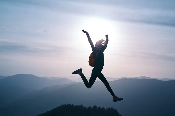 Mulher pulando na montanha no céu por do sol e montanhas fundo — Fotografia de Stock