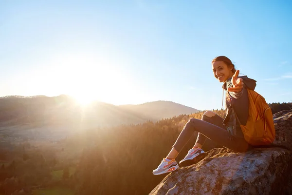 Femme souriante randonneur assis sur le bord de la falaise sur fond de lever de soleil — Photo