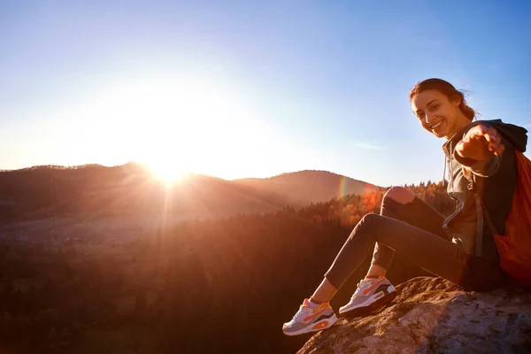 微笑的女人徒步者坐在悬崖边的背景下日出 — 图库照片