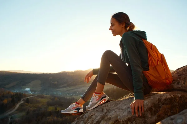 Woman sits on edge of cliff against background of sunrise — Stock Photo, Image