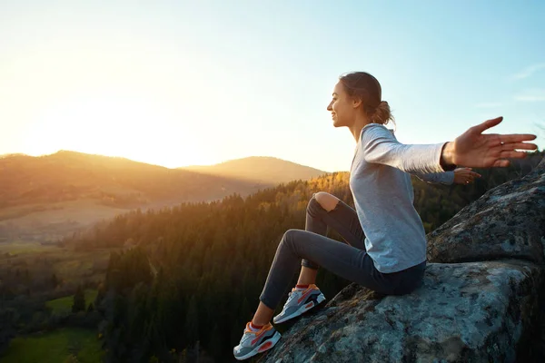 Junge Frau sitzt am Rand der Klippe vor dem Hintergrund des Sonnenaufgangs — Stockfoto