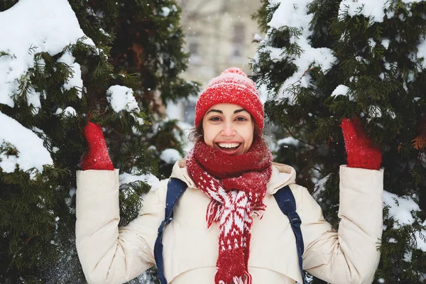 在城市暴风雪过后 穿着白色羽绒服 红色帽子 围巾和手套的欢快微笑妇女 在雪域小巷里用小云杉描绘 复制空间 — 图库照片