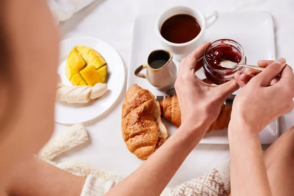 Chica en camiseta blanca sentada en la cama y desayunando —  Fotos de Stock