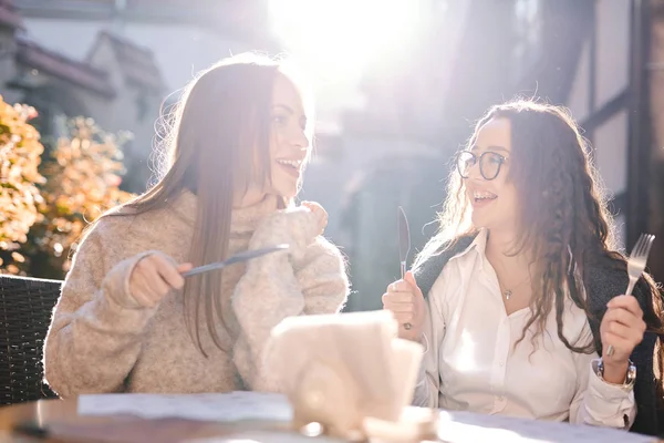 Twee mooie modieuze vrouwen zitten in de straat café, lachen en plaing — Stockfoto