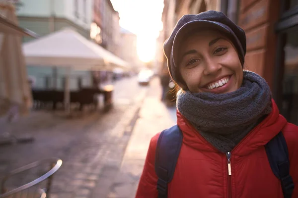 Jeune femme en veste rouge et casquette grise marchant dans la rue le soir — Photo