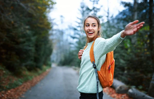 Mujer excursionista con mochila pequeña, de pie en la carretera en el bosque —  Fotos de Stock