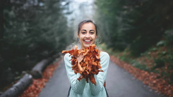 Retrato de una mujer feliz jugando con hojas de otoño en el bosque — Foto de Stock