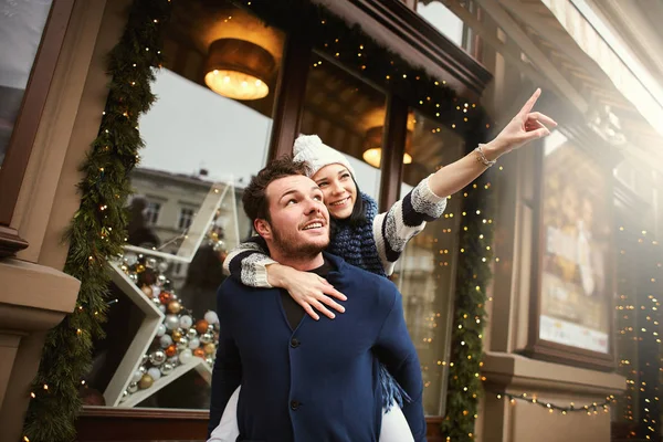 Amantes hombre y mujer de pie abrazándose en el fondo de un escaparate de Navidad decorado y mirar hacia otro lado —  Fotos de Stock
