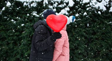 mutlu sarılma iki sıcak kış giysileri içinde açık havada kırmızı balon şeklinde bir kalple duruyor