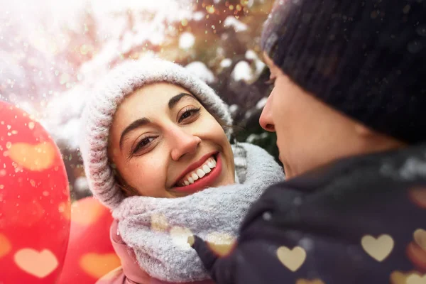 Feliz abrazo pareja en caliente invierno ropa es de pie al aire libre con un corazón en forma de globo rojo —  Fotos de Stock