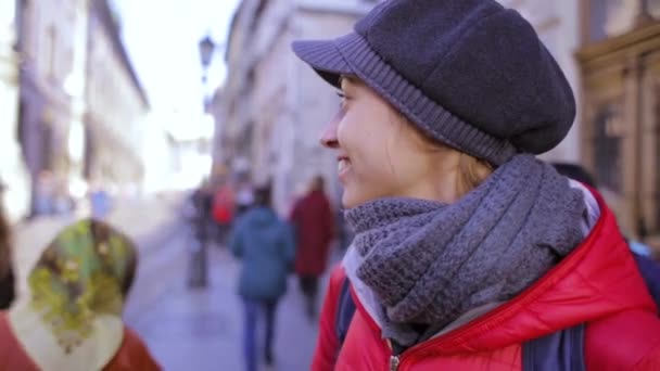 Mujer joven con chaqueta roja y gorra gris caminando por la calle — Vídeos de Stock