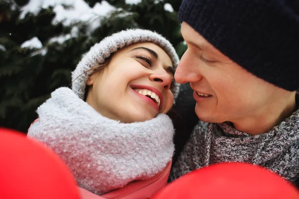 Felice coppia di abbracci in abiti invernali caldi è in piedi all'aperto con un palloncino rosso a forma di cuore — Foto Stock