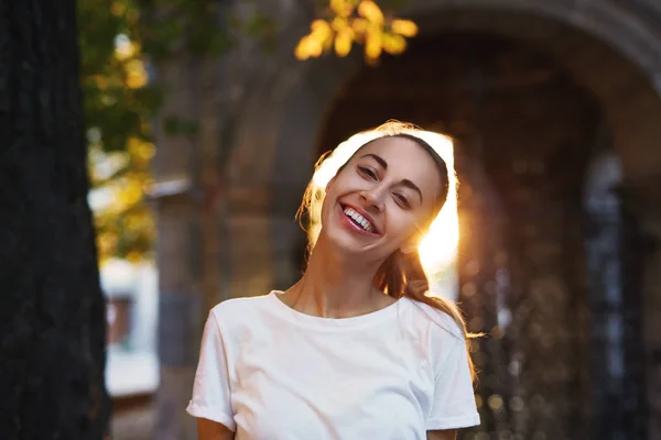 Retrato de una joven atractiva y sonriente mujer de pie en la calle con una luz del atardecer —  Fotos de Stock