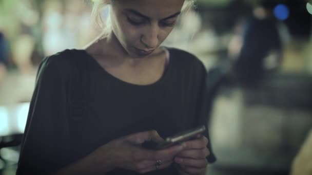 Jonge vrouw staat buiten 's nachts in de stad met behulp van de telefoon. — Stockvideo