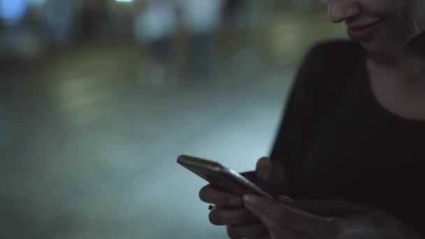 Genç kadın telefonu kullanarak şehirde geceleri açık havada duruyor. — Stok video