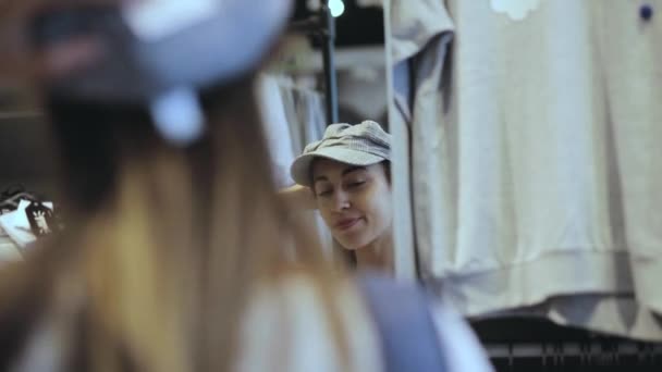 Una joven se prueba un sombrero en una tienda frente al espejo — Vídeos de Stock